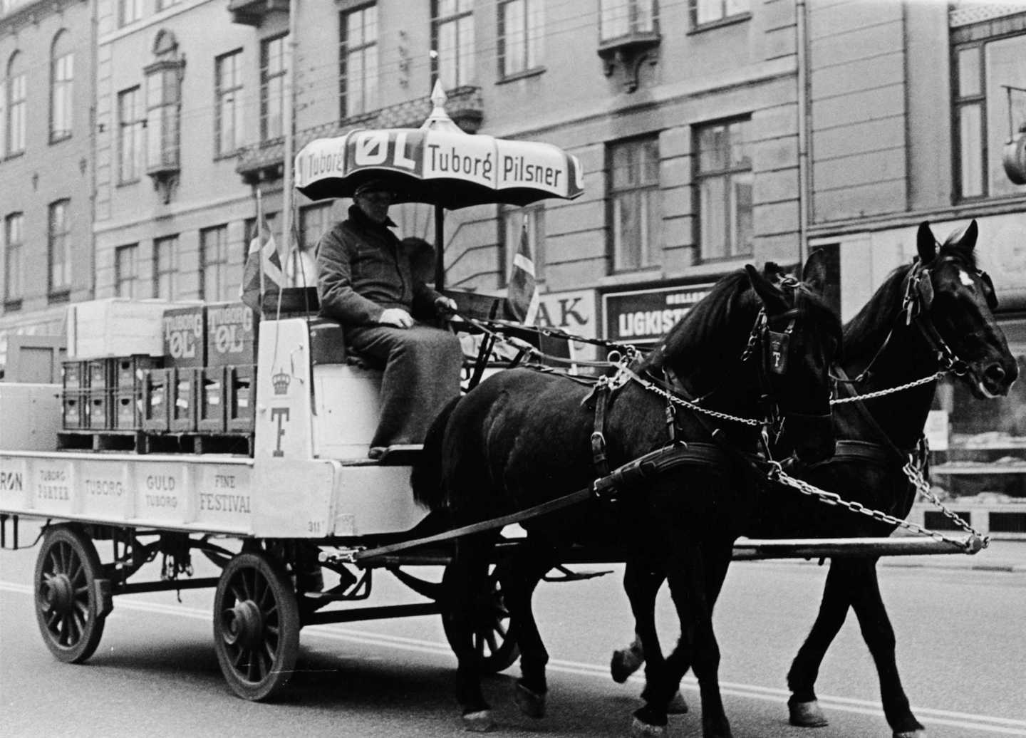 Ølvogn med to forspændte heste. Over kusken er en parasol med reklamer for Tuborg.