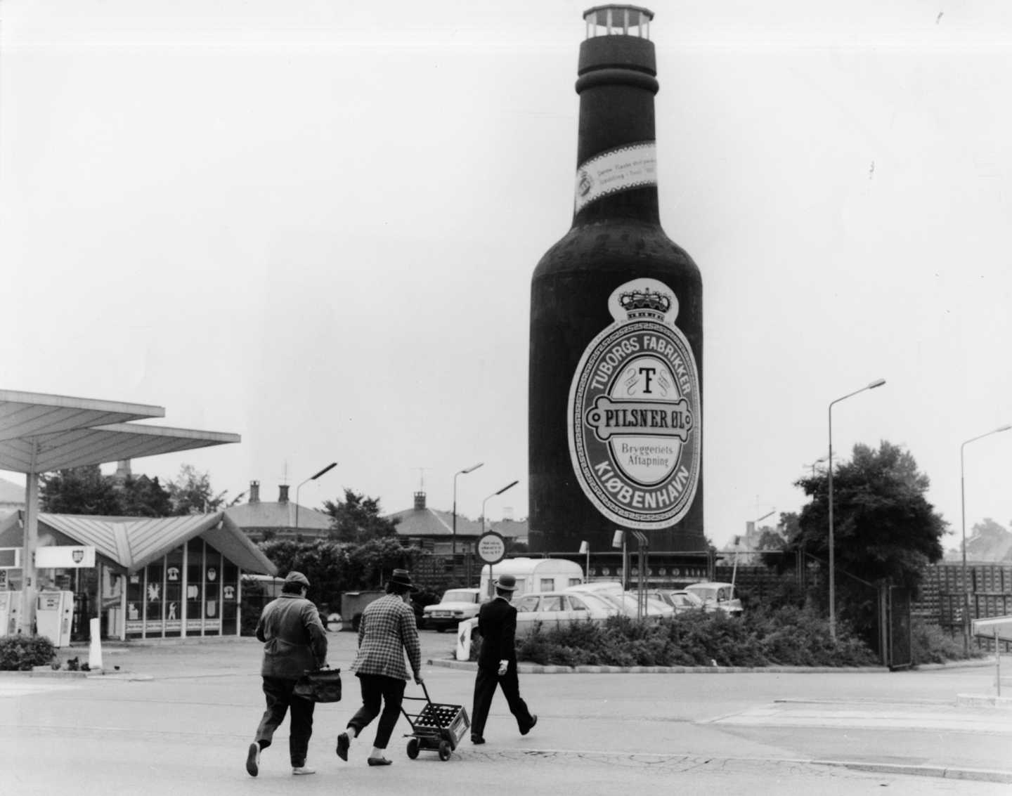 Foto fra Olsen-banden film. Kjeld, Benny og Egon går på række hen mod den store Tuborgflaske.