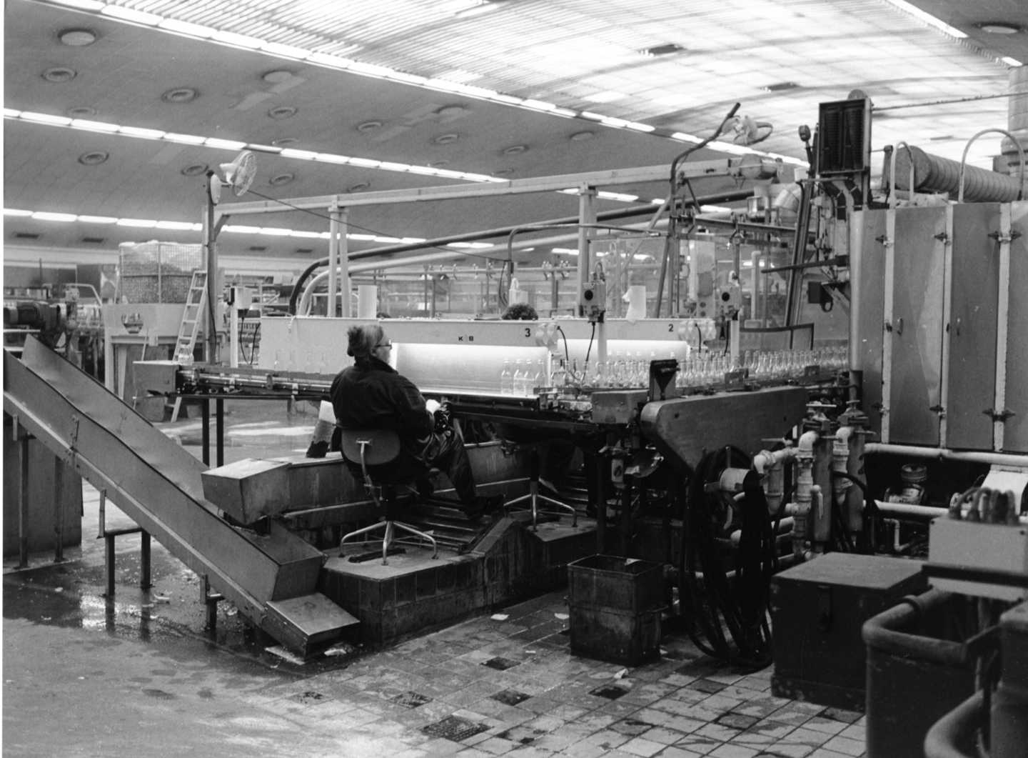 Tuborgs Tappehal, hvor en kvinde sidder med ryggen til og overvåger samlebånd med flasker.