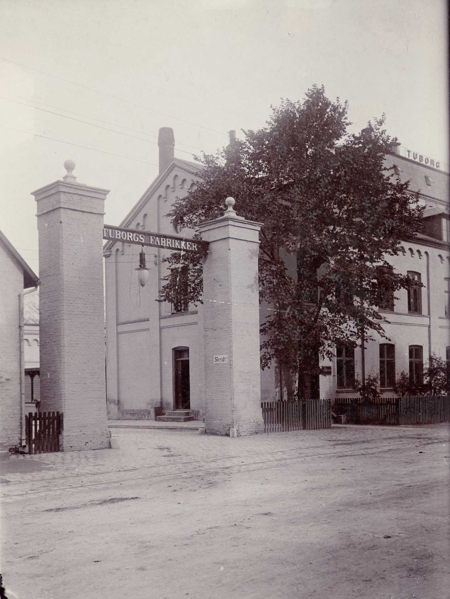 Indkørslen til Tuborgs Fabrikker fra Strandvejen, ca. 1900. Porten består af to murede søjler og en overligger med teksten "Tuborgs Fabrikker""
